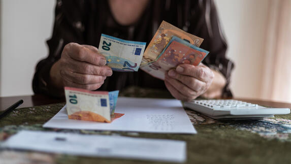 Persoon zit aan tafel met daarop een rekenmachine en papieren terwijl zij eurobiljetten telt.